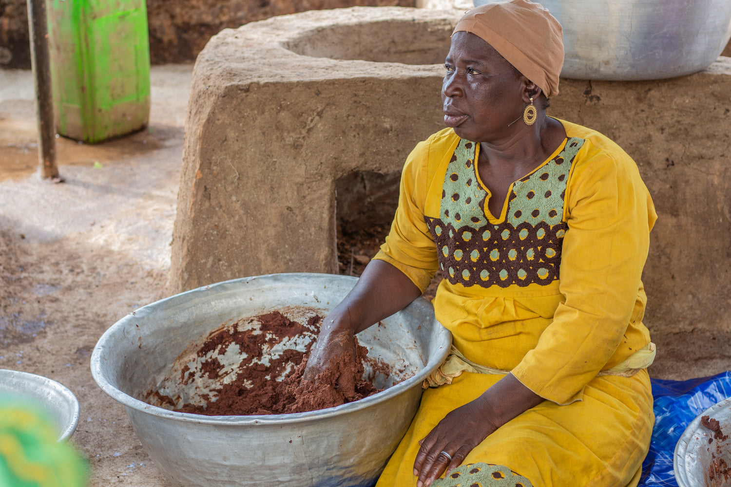 A Ghanaian woman is sitting mixing Shea with her hands. The shea is in a bowl next to it.